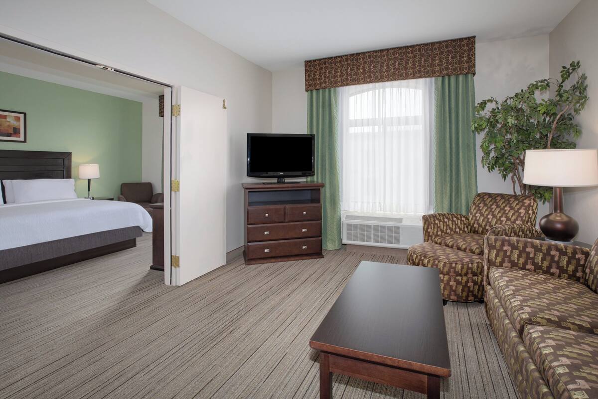 A hotel room with a bed, a television on a dresser, a sofa, a coffee table, and a plant.