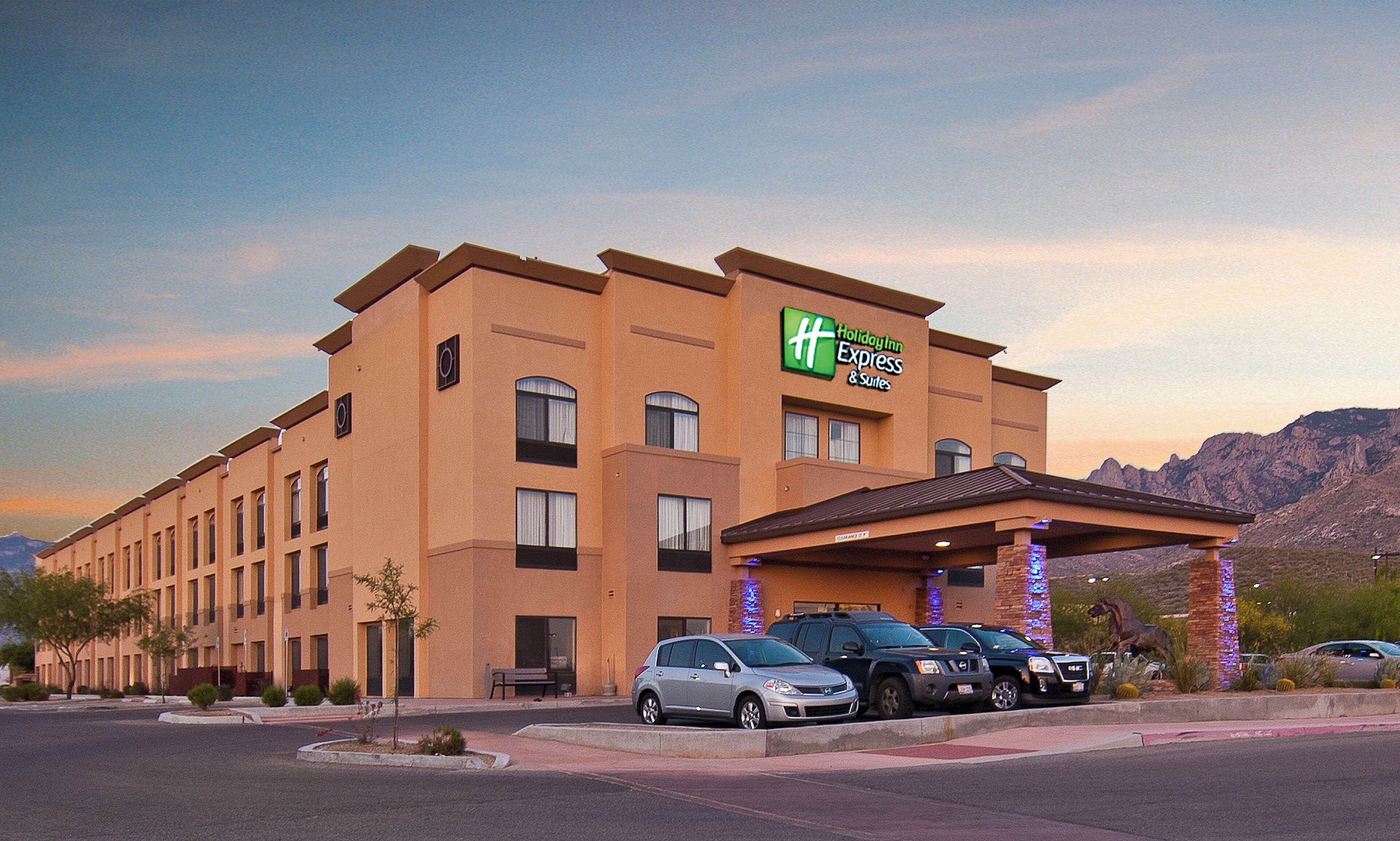 Edificio de Holiday Inn Express con estacionamiento y montañas al fondo.