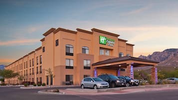 Edificio de Holiday Inn Express con estacionamiento y montañas al fondo.
