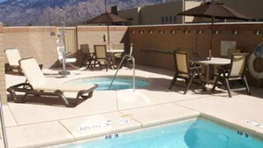 An outdoor pool area with lounge chairs and umbrellas, surrounded by a brick wall and mountains in the background. - Holiday Inn Express & Suites Oro Valley-Tucson North by IHG (Oro Valley)