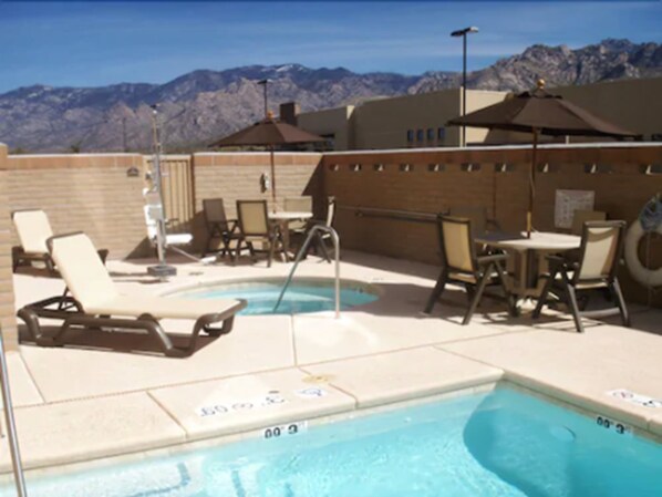 An outdoor pool area with lounge chairs and umbrellas, surrounded by a brick wall and mountains in the background. - Holiday Inn Express & Suites Oro Valley-Tucson North by IHG (Oro Valley)