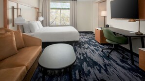 A hotel room with a bed, a sofa, a desk, a chair, a TV, and a window with curtains. - Fairfield Inn & Suites by Marriott Rome (Rome)
