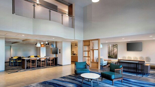 A spacious lobby with a high ceiling, a mezzanine level, a seating area with a sofa and chairs, a small table, and a television mounted on the wall. - Fairfield Inn & Suites by Marriott Rome (Rome)