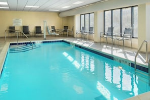 Une piscine intérieure à l’eau claire, dotée d’un indicateur de profondeur et de grandes fenêtres baignées de lumière.