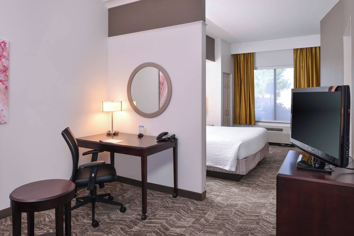 A hotel room with a bed, a desk with a lamp, a chair, a television, and a large window with curtains.