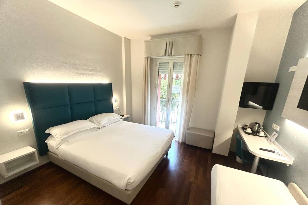 A hotel room with a bed, bedside table, and a desk with a chair.