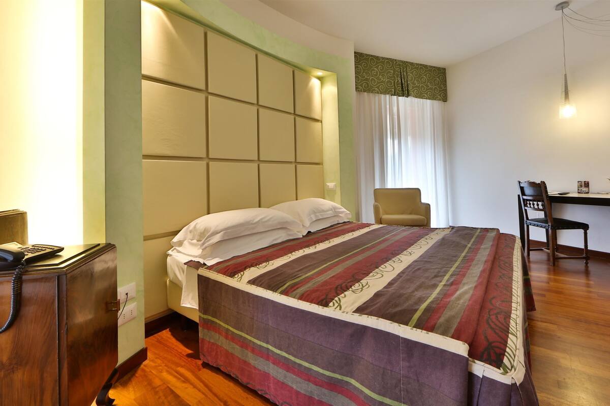 A hotel room with a bed, a desk, a chair, and a telephone.