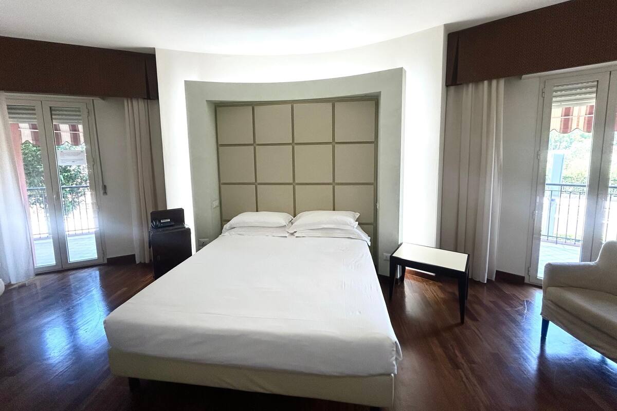 A hotel room with a large bed, a bedside table, a chair, and a view of the outside.
