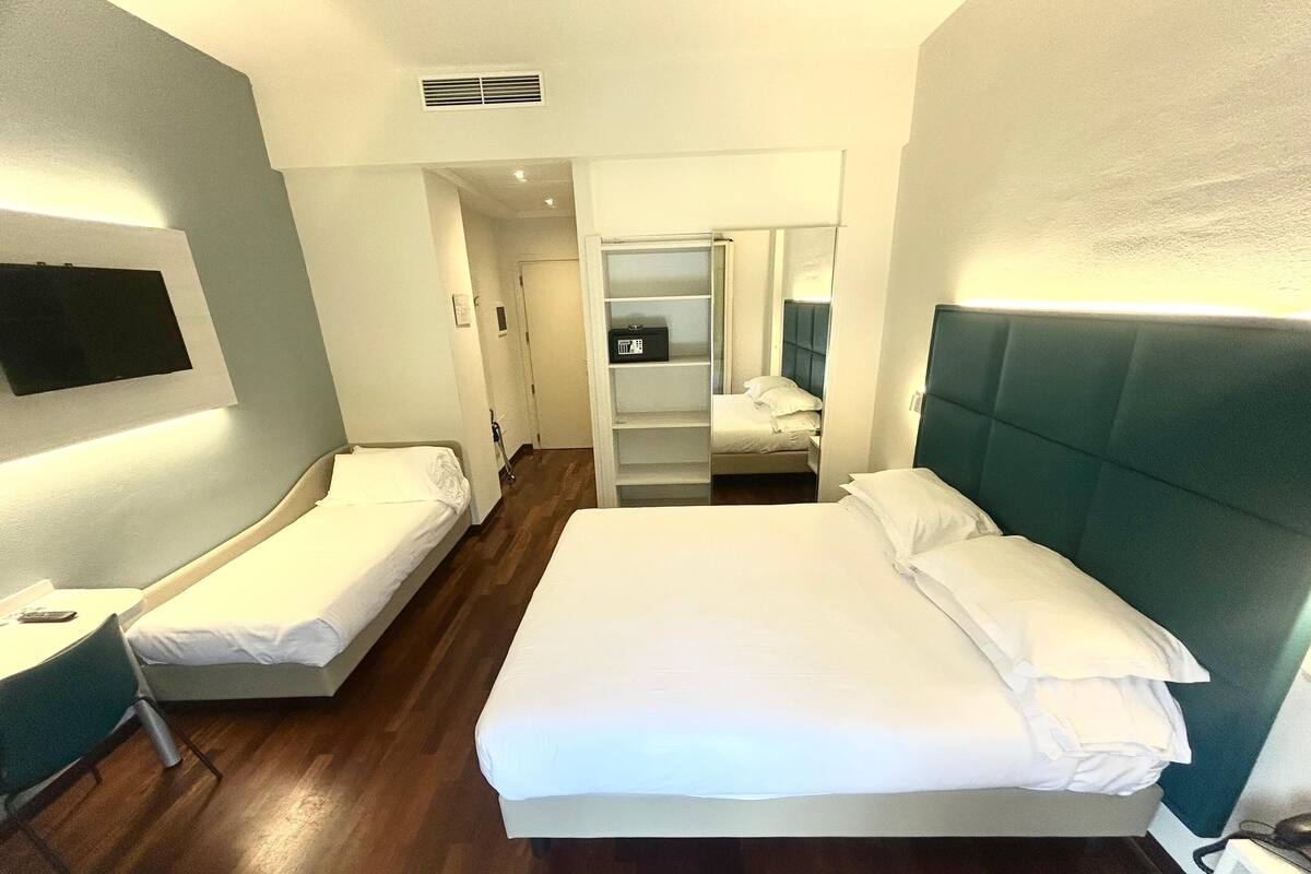 A hotel room with two single beds, a desk, a chair, and a TV.