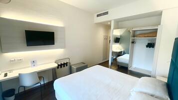 Ein Hotelzimmer mit Bett, Schreibtisch, Stuhl, Fernseher und Kleiderschrank.