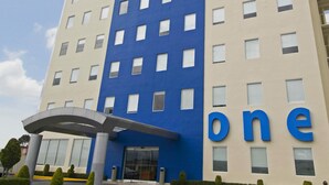 Een hotel met meerdere verdiepingen, een blauw en beige gevel, een opvallend 'one' bord en een overdekte ingang.