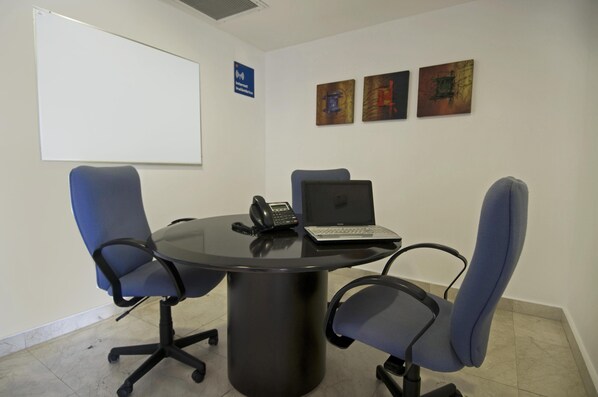 Une salle de conférence équipée d’une table ronde, de quatre chaises de bureau, d’un ordinateur portable, d’un téléphone et d’un tableau blanc.