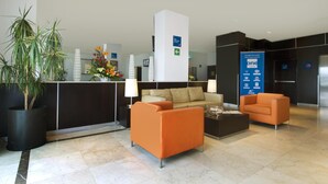 Een moderne hotellobby met een receptiebalie, een zithoek en een groot blauw bord.