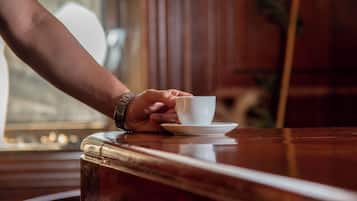 A hand holding a cup on a wooden table with a window in the background.