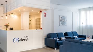 A hotel reception area with a white reception desk, blue sofas, and a modern chandelier.
