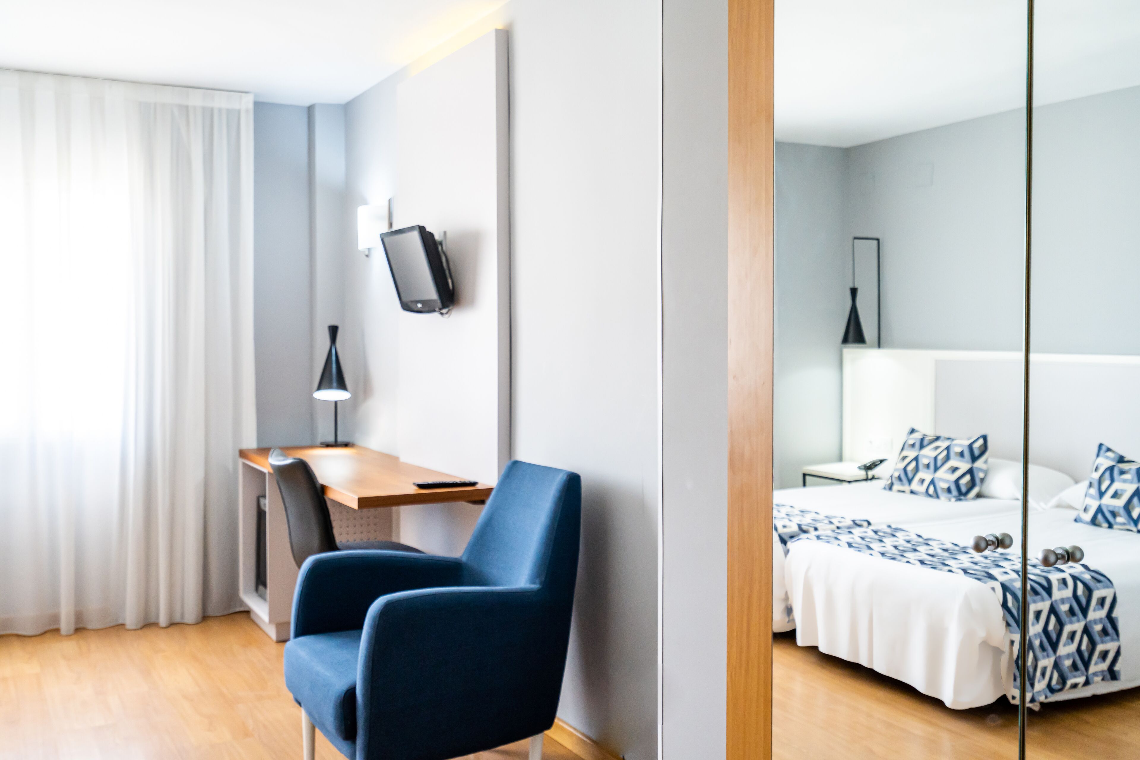 Una habitación de hotel moderna con escritorio, silla y cama con ropa de cama estampada.