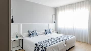 Un dormitorio moderno con una cama grande, paredes blancas y una ventana con cortinas translúcidas.