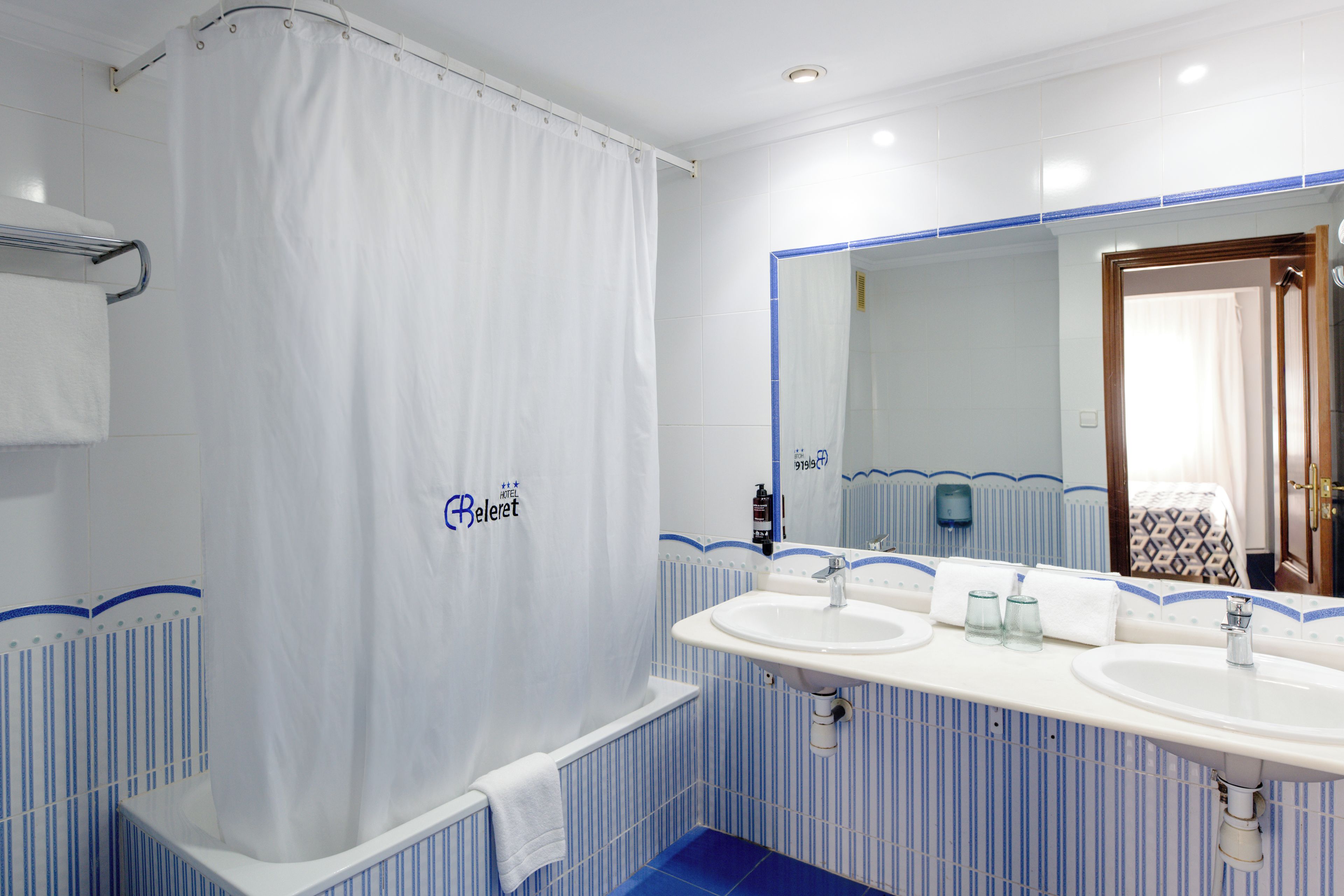 A hotel bathroom with a shower curtain, two sinks, and a mirror.