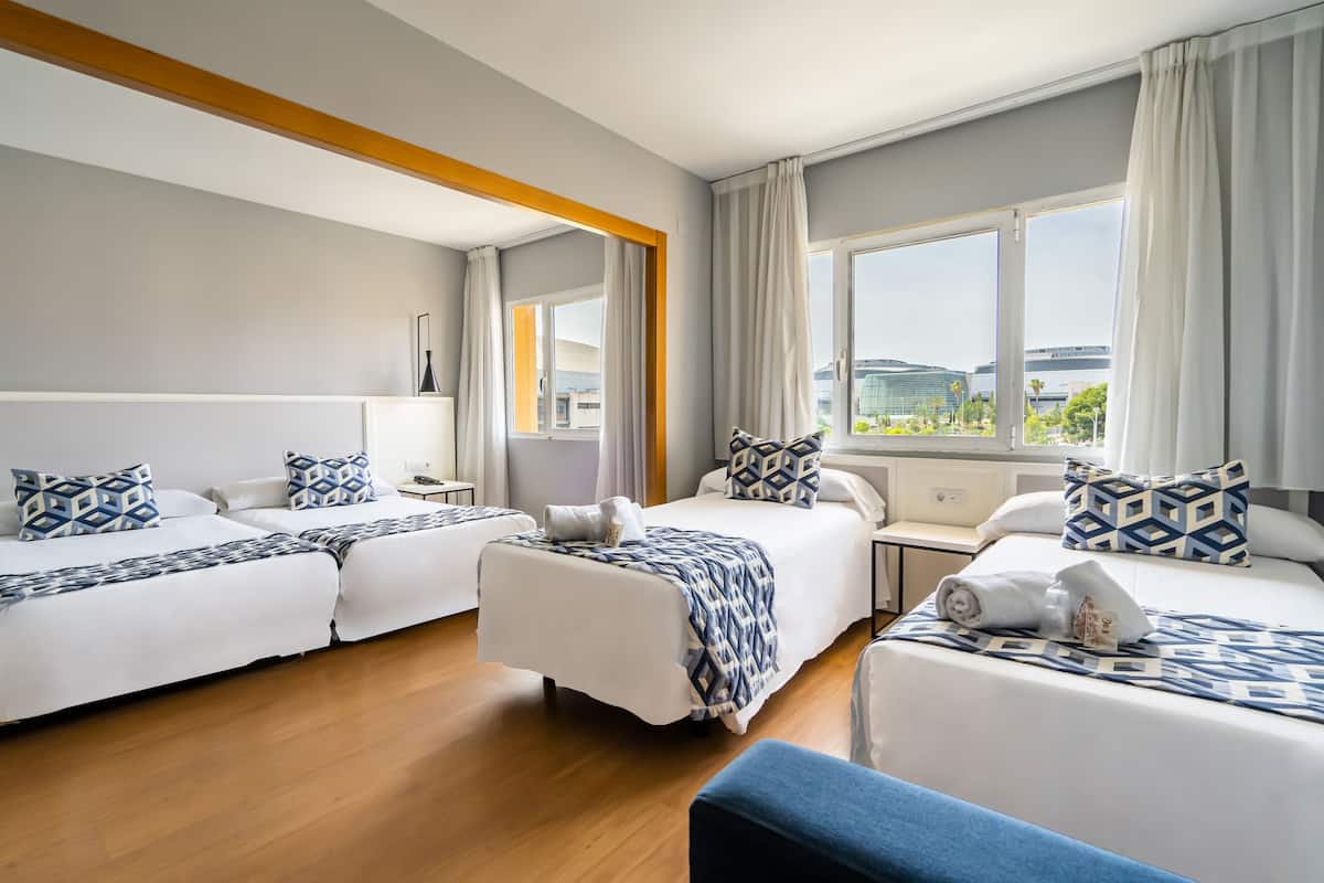 A hotel room with two beds, a desk, and a window with a city view.