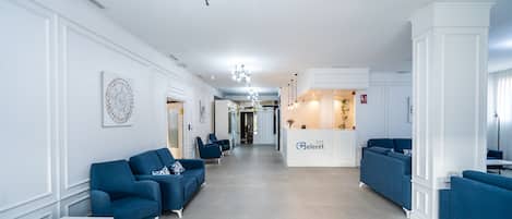 A spacious lobby with blue sofas, a reception desk, and a modern chandelier.