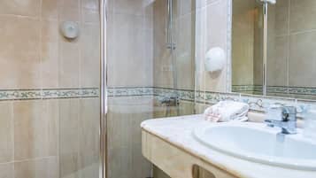 Un baño con ducha de vidrio, lavamanos con espejo y un perchero para toallas.