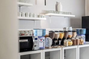 Un área de cocina con estantes que sostienen tazas y vasos, un dispensador de agua y varios recipientes para almacenar alimentos.