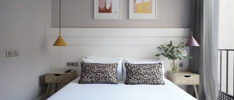 A modern hotel room with a large bed, two bedside tables, a nightstand, a vase with flowers, and two abstract paintings on the wall.