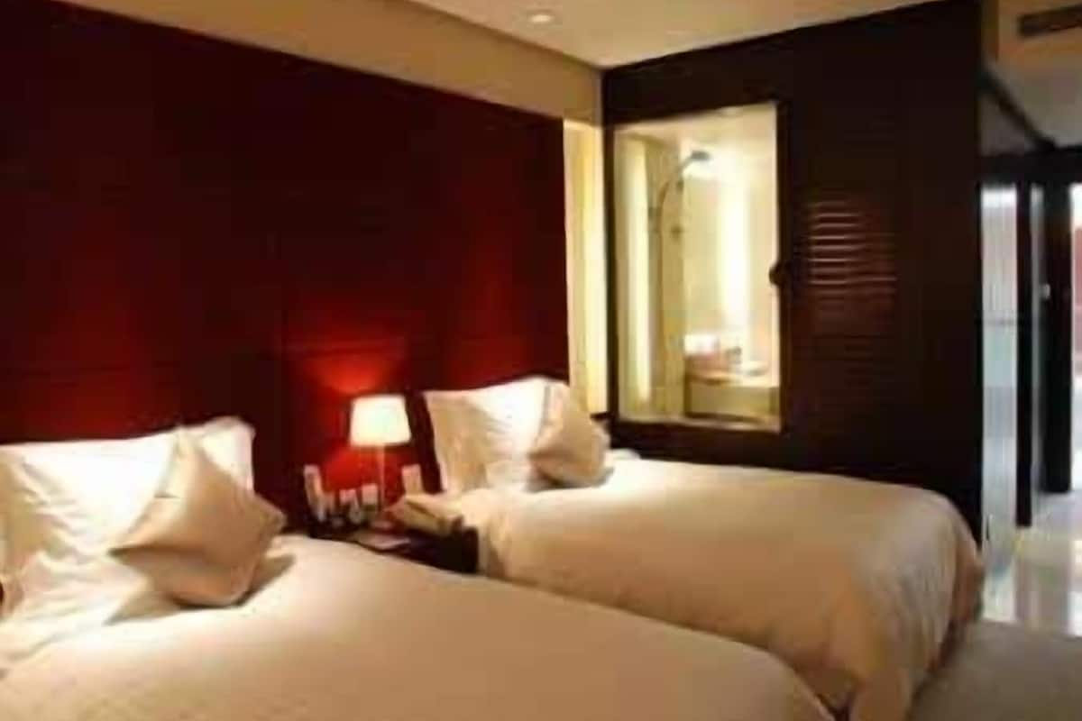 Habitación de hotel con dos camas, una mesita de noche y una ventana con vista al interior.