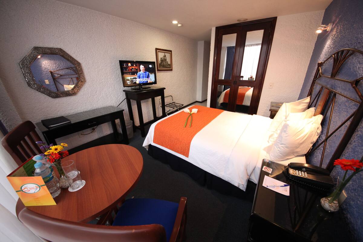 Ein Hotelzimmer mit einem Bett, einem Schreibtisch mit Fernseher, einem Esstisch mit Stühlen und einer Vase mit Blumen.