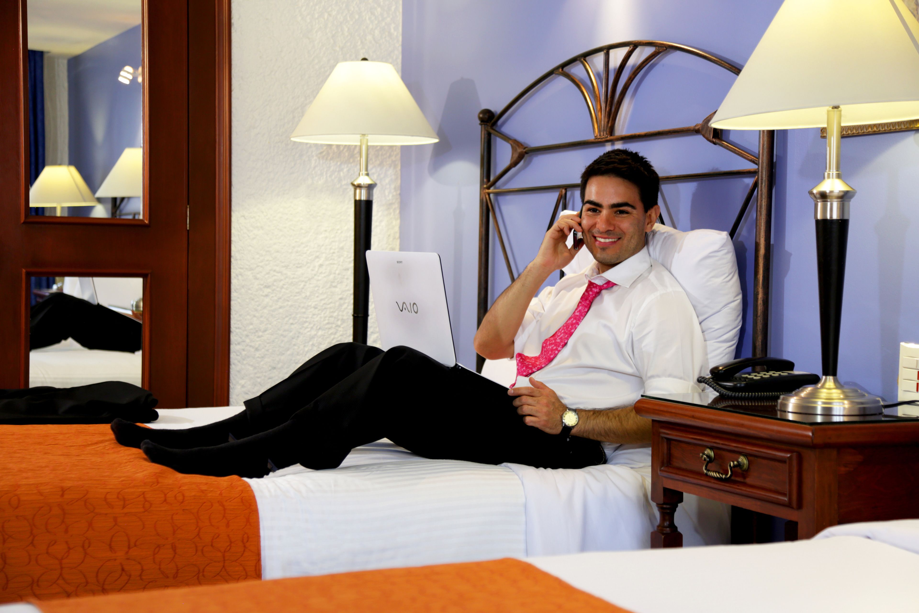 A hotel room with a bed, a bedside table with a lamp, and a mirror on the wall.