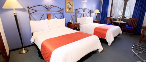 Habitación de hotel con dos camas, un escritorio, sillas y una ventana con cortinas.