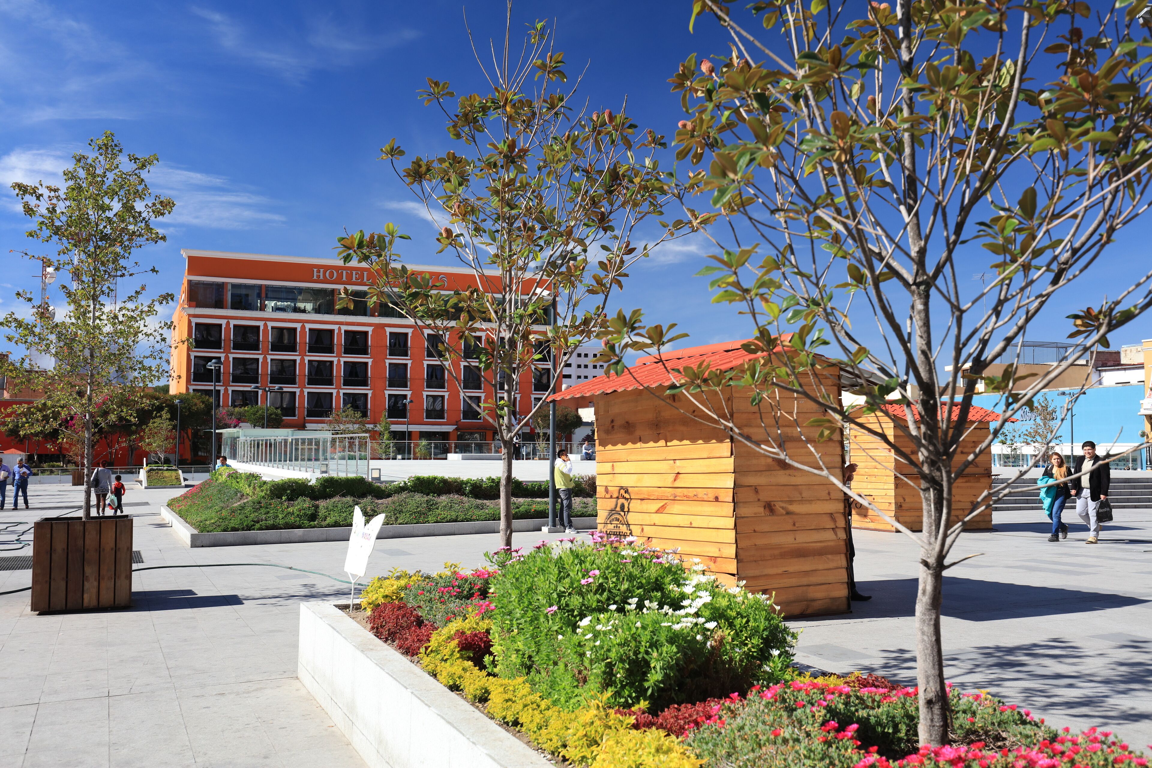 Hotel amb façana vermella, estructura de fusta i jardí paisatjistic ple de plantes i flors diverses.