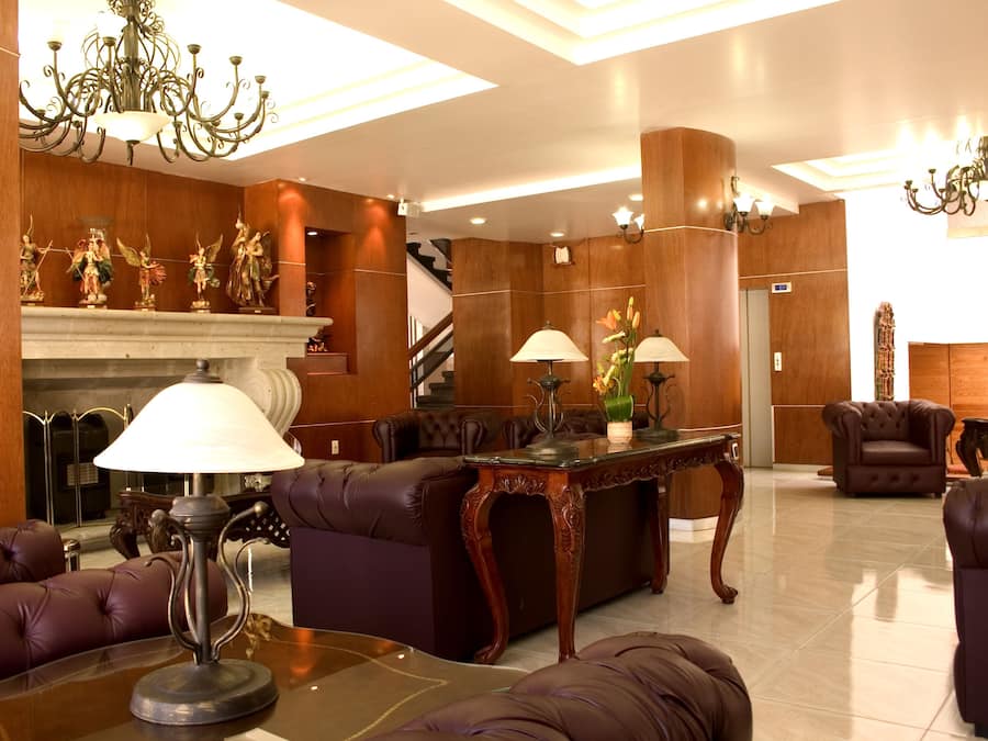 Un vestíbulo con sofás de cuero, chimenea, candelabros y una escalera.