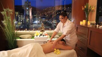 A massage therapy room with a cityscape view, a massage table, and a decorative vase with flowers.