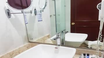 Un baño con un lavamanos blanco, un espejo redondo, una ducha con cerramiento de vidrio y un secador de pelo en la encimera.