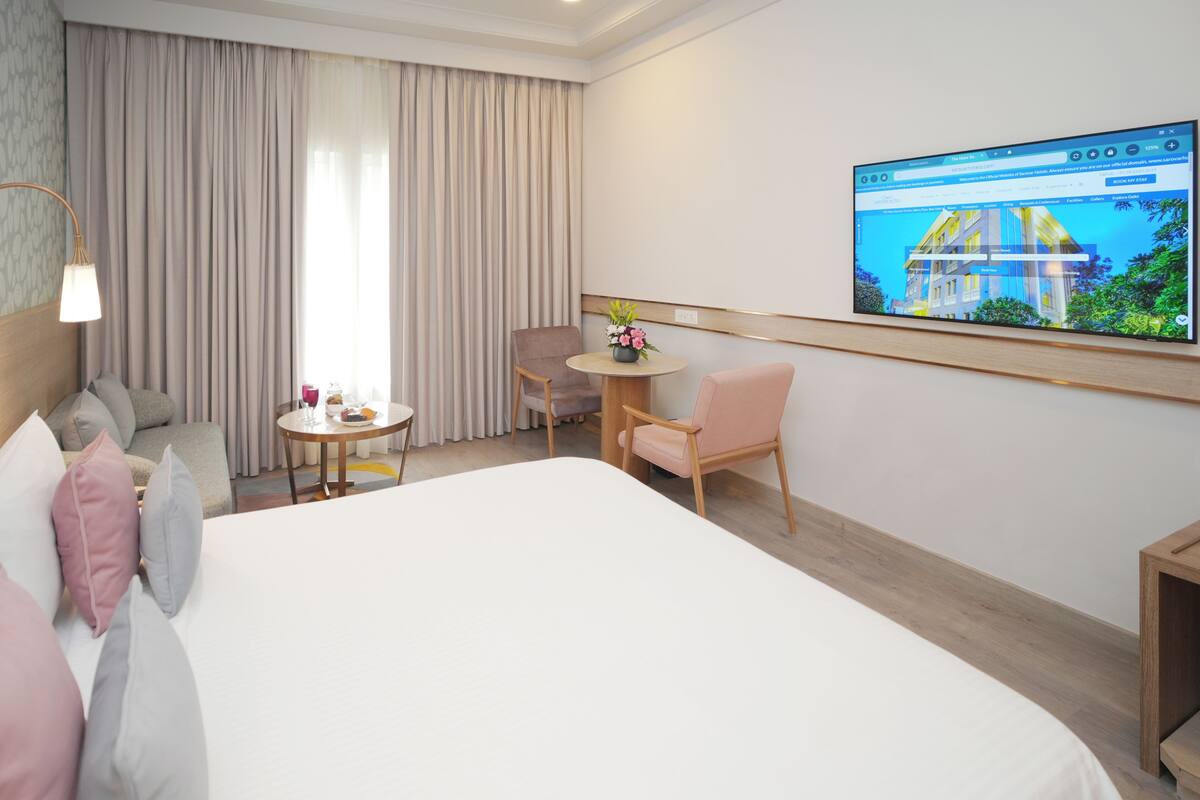 A hotel room with a bed, a desk, a chair, a TV on the wall, and a window with curtains.