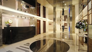 A spacious lobby with a central reflective black circular area, a reception desk, and a large floral arrangement.