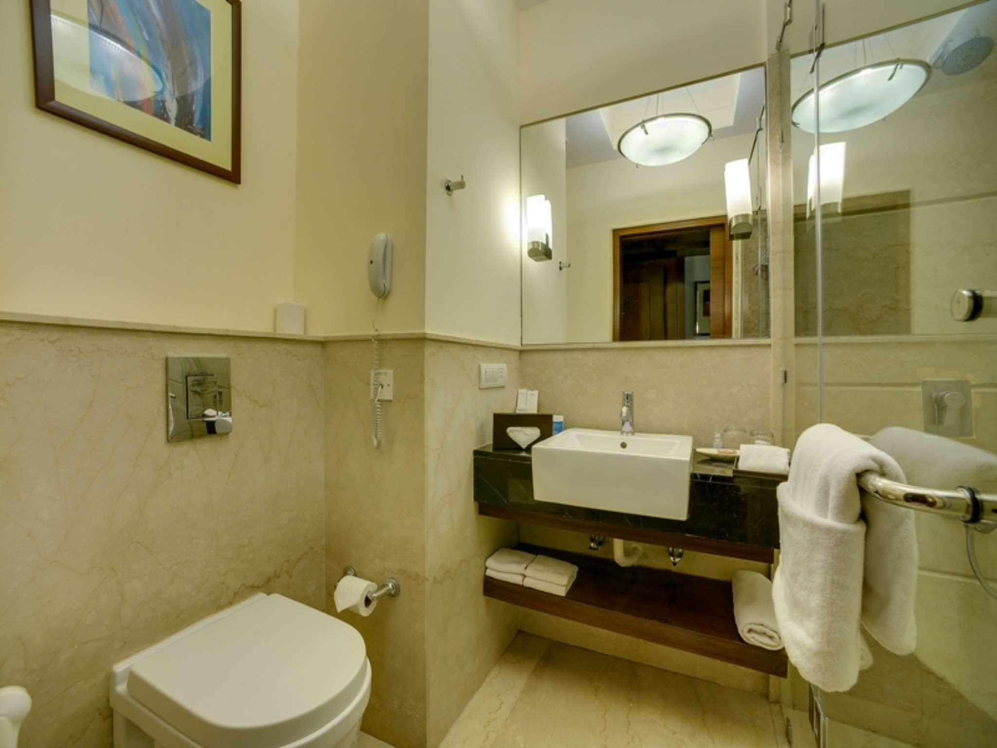 Et badeværelse med toilet, vask, spejl og håndklæderadiator.
