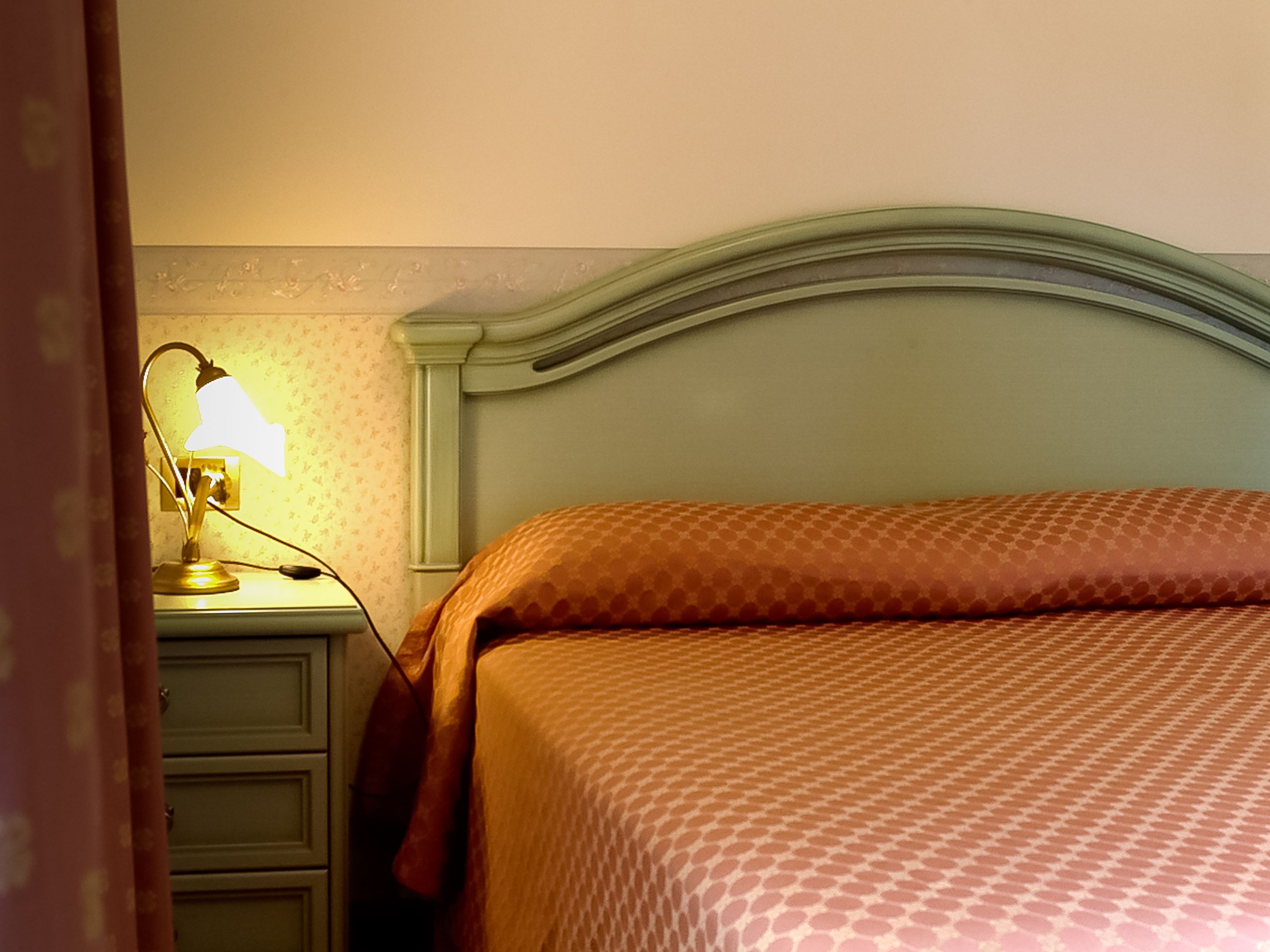 A neatly made bed with a patterned bedspread, a bedside lamp, and a nightstand with a drawer.