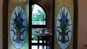 En døråbning med frostede glaspaneler med blomstermotiver, der fører til et spiseområde med et bord dækket til to personer og udsigt til grønne omgivelser udenfor.