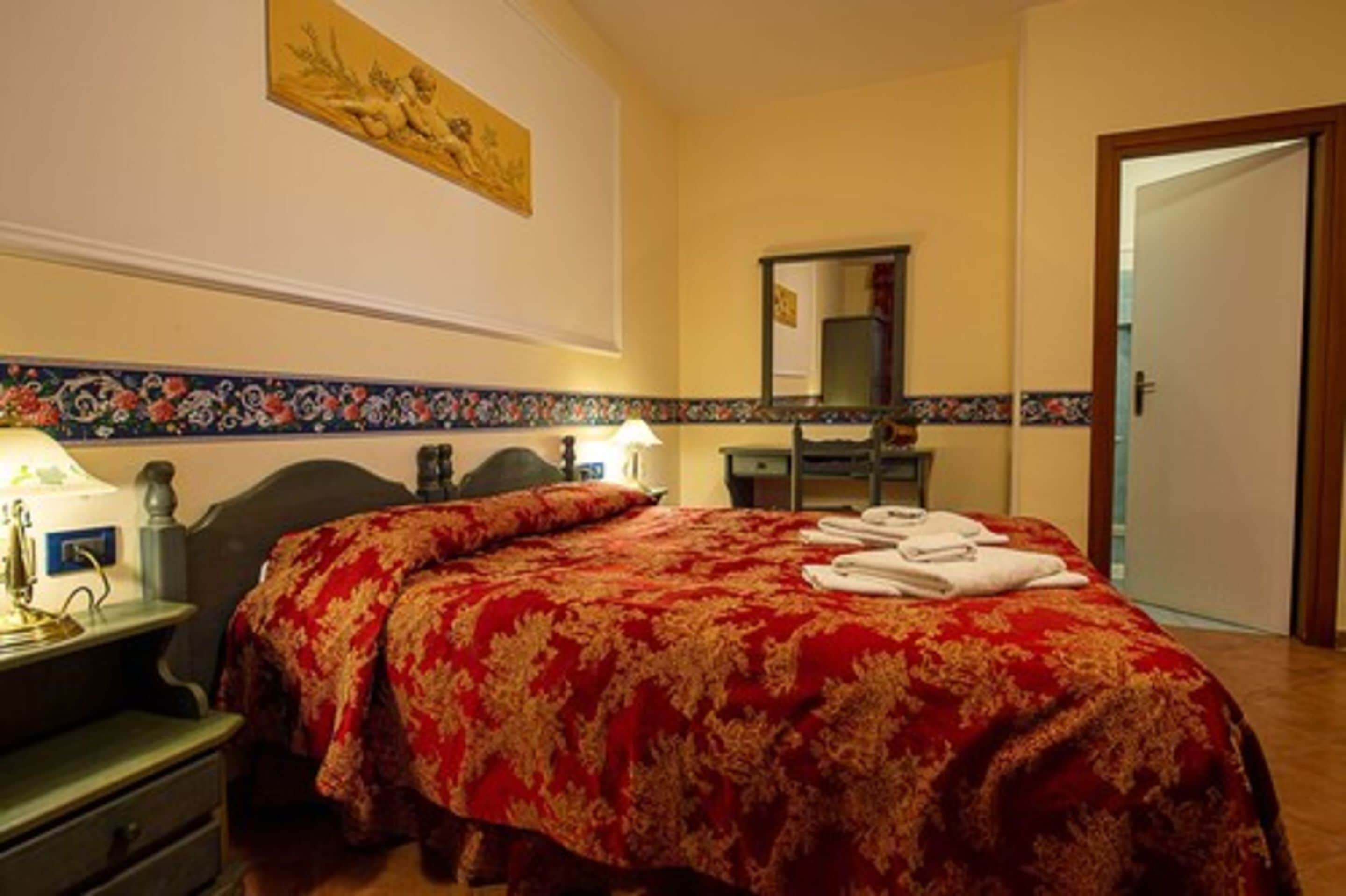 A hotel room with a large bed, a bedside table, a lamp, a mirror, and a door.