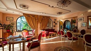 En rummelig lounge med røde og gyldne møbler, et stort vindue med gardiner og et loft med dekorative mønstre.