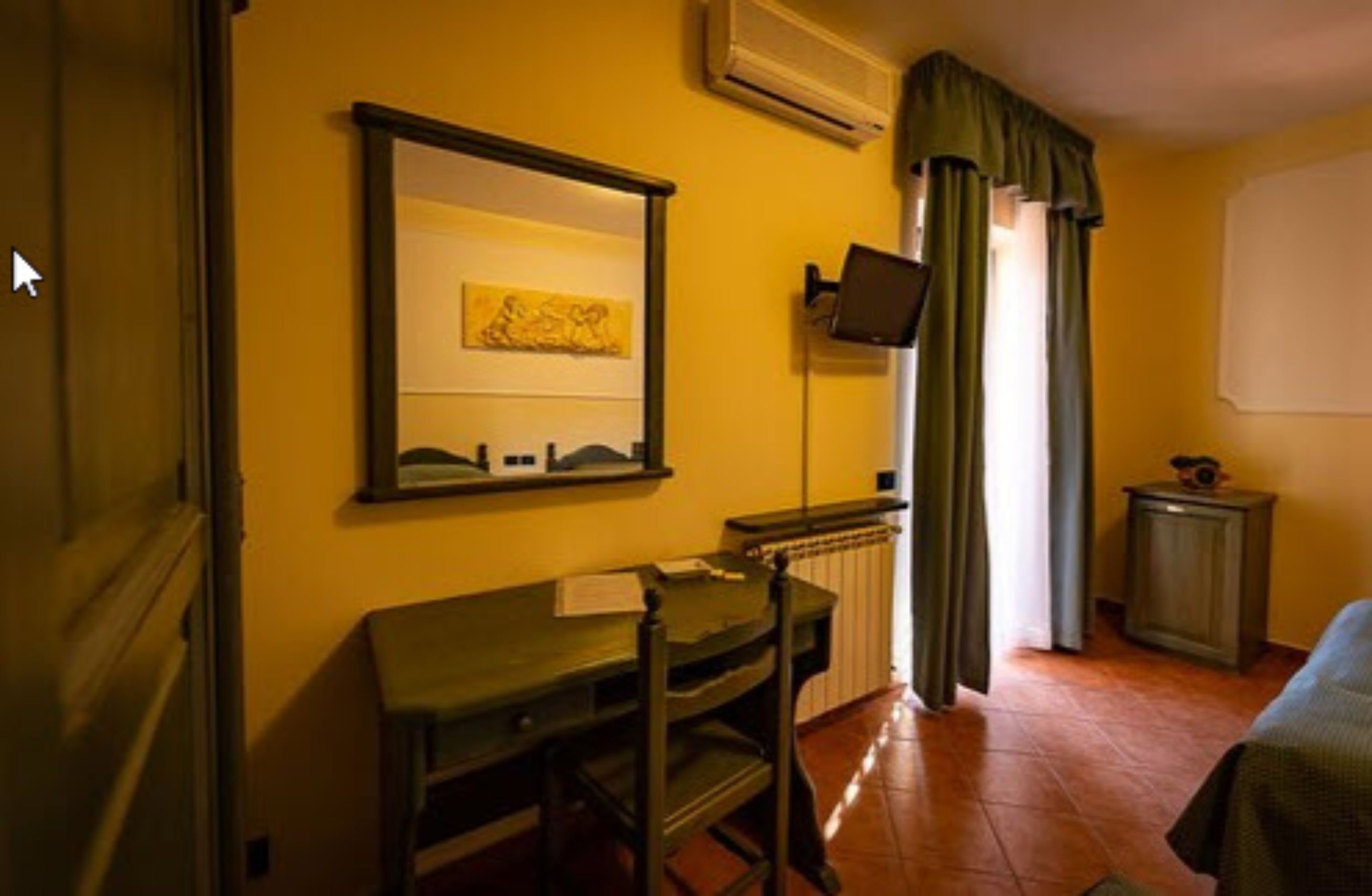 A room with a desk, chair, and a television mounted on the wall.