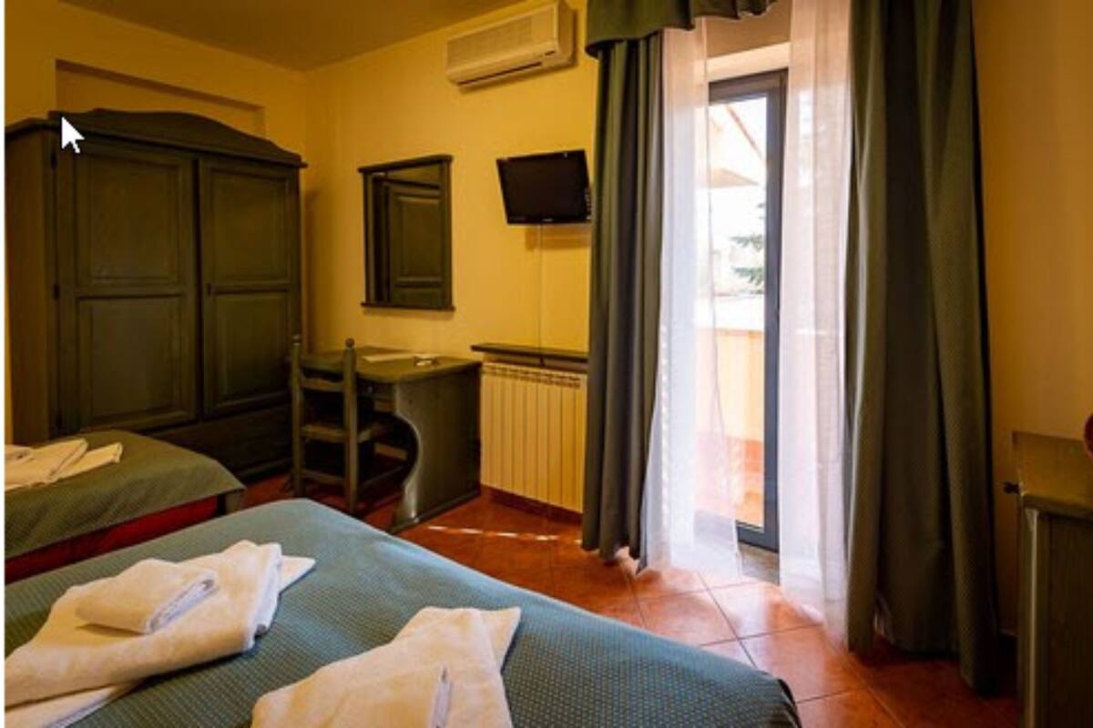 Une chambre d’hôtel avec deux lits, un bureau, une chaise, une télévision et une fenêtre avec des rideaux.