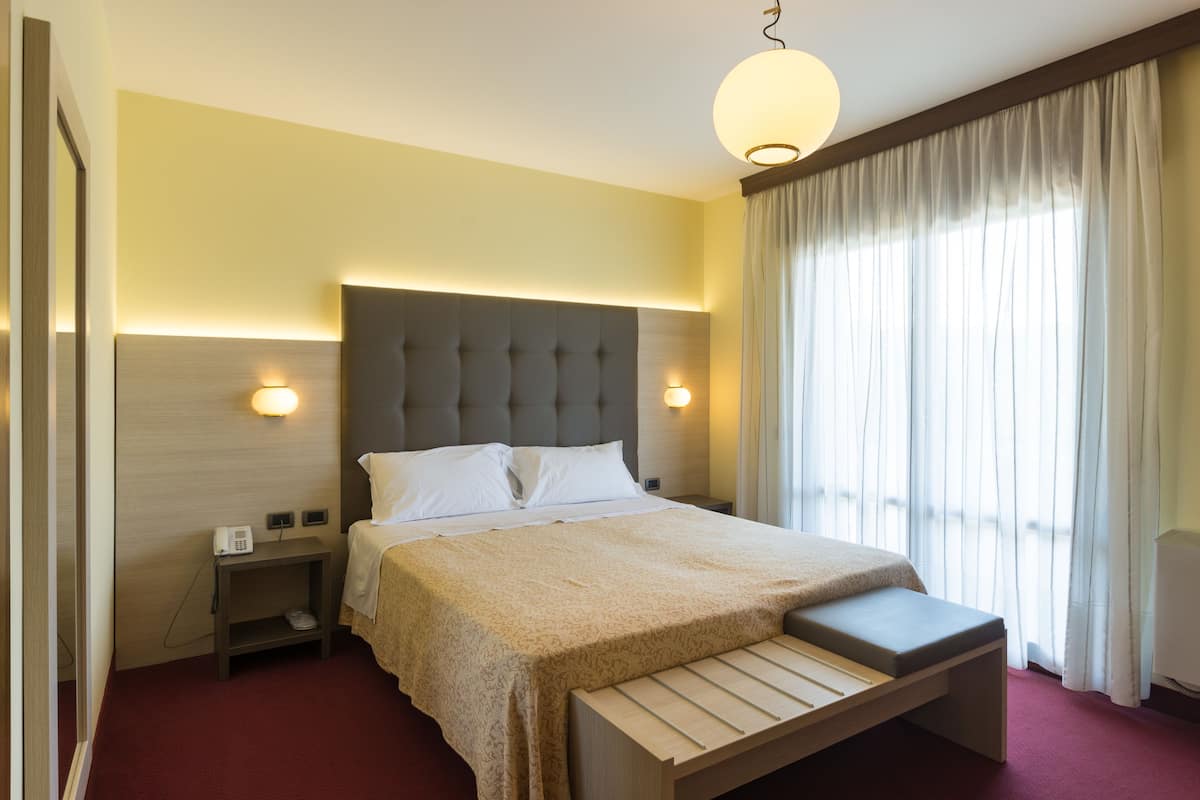 A hotel room with a large bed, bedside tables, a bedside lamp, and a window with curtains.