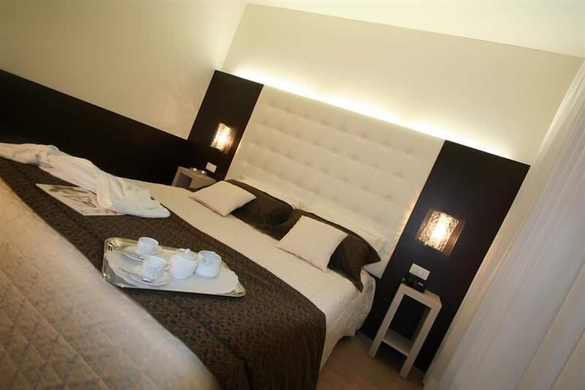 A hotel room with a large bed, a bedside table, and a tray with tea cups and saucers.