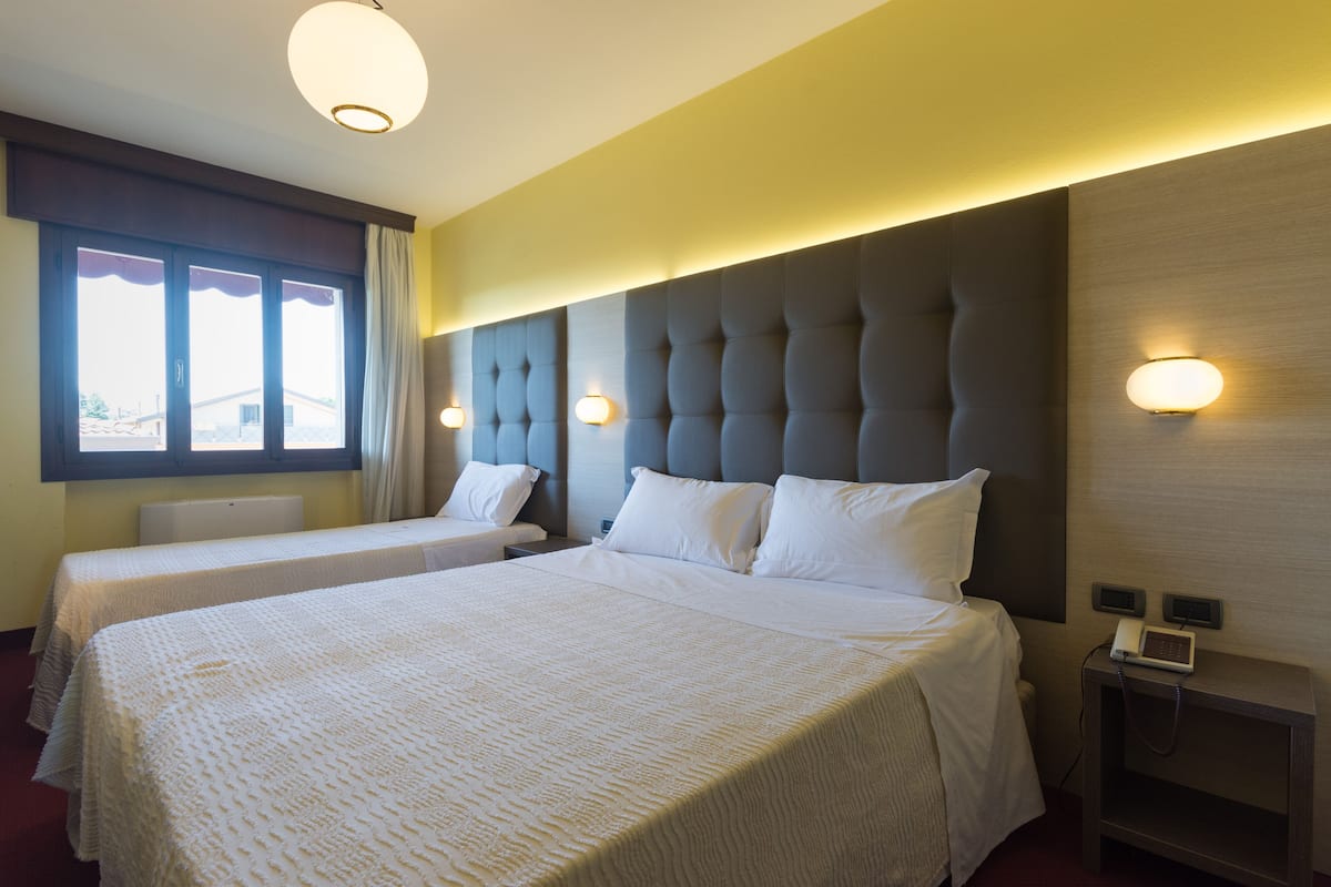 A hotel room with two beds, a large window, and a bedside table with a phone.