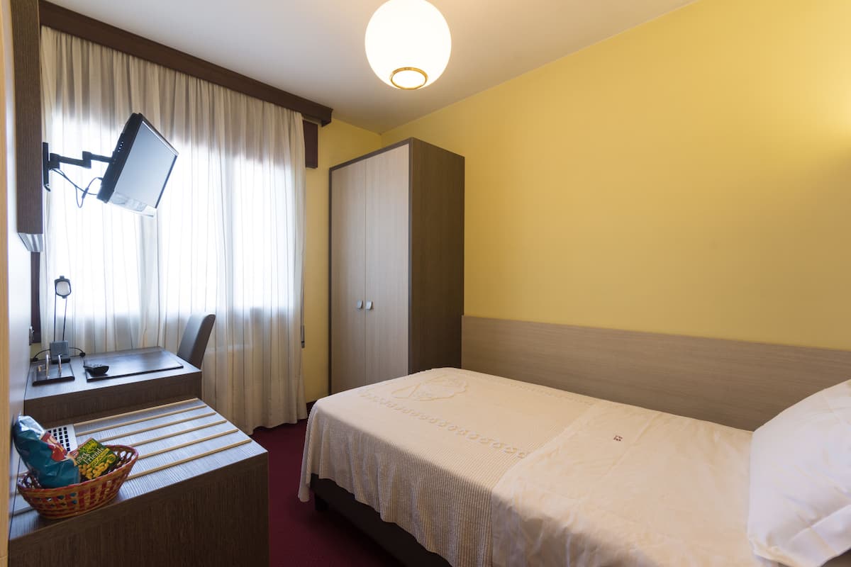 A hotel room with a bed, a desk with a computer, a chair, a wardrobe, and a window with curtains.