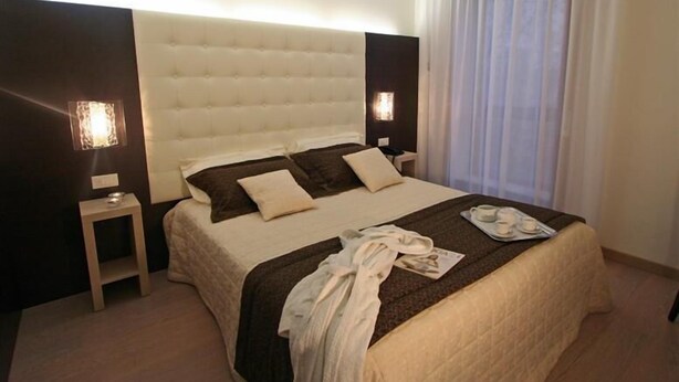 A hotel room with a large bed, two bedside tables, a nightstand, a window with curtains, and a wall-mounted light fixture. - Park Hotel Ristorante Ca' Bianca (Istrana)