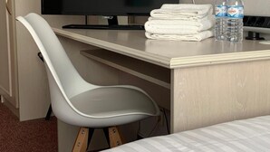 Habitación de hotel con cama, escritorio con televisor, silla blanca y dos botellas de agua.